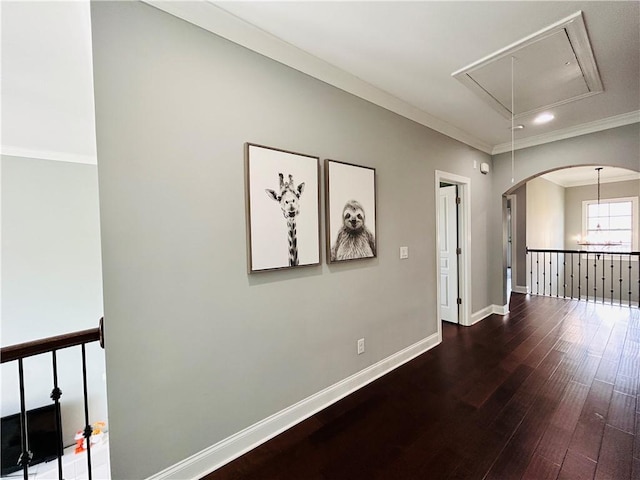 corridor with attic access, crown molding, arched walkways, wood finished floors, and baseboards