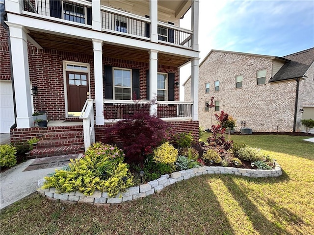 view of exterior entry featuring a lawn, a porch, brick siding, and a balcony