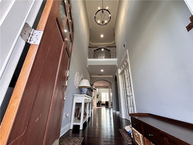 foyer entrance with an inviting chandelier, wood finished floors, baseboards, a high ceiling, and arched walkways
