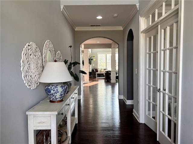 hallway with crown molding, visible vents, dark wood-style flooring, ornate columns, and arched walkways