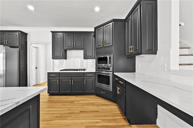 kitchen featuring light stone counters, tasteful backsplash, light wood-style floors, and appliances with stainless steel finishes