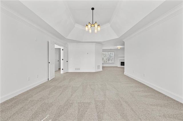 unfurnished living room with a tray ceiling, carpet floors, a fireplace, crown molding, and a chandelier