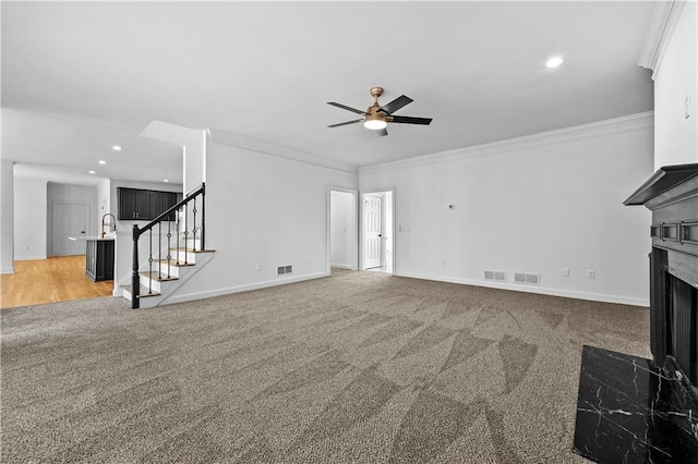 unfurnished living room featuring visible vents, a fireplace with flush hearth, light carpet, stairway, and crown molding