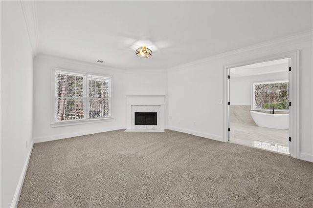 unfurnished living room featuring a high end fireplace, baseboards, crown molding, and carpet