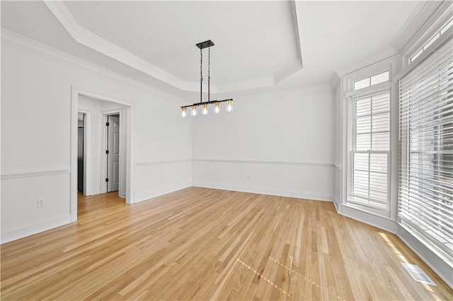 unfurnished dining area with a raised ceiling, crown molding, light wood-type flooring, and baseboards