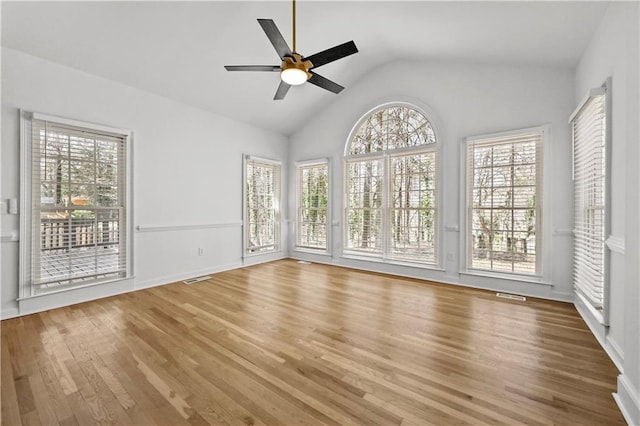 empty room featuring vaulted ceiling, wood finished floors, visible vents, and a healthy amount of sunlight