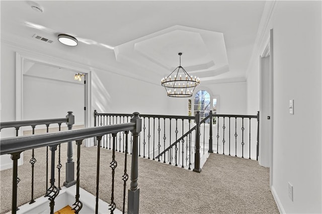 hallway featuring visible vents, a raised ceiling, carpet flooring, an upstairs landing, and a chandelier