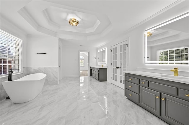 full bath with two vanities, a sink, french doors, a raised ceiling, and a freestanding bath