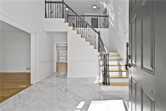 foyer entrance featuring visible vents, marble finish floor, stairs, and a high ceiling