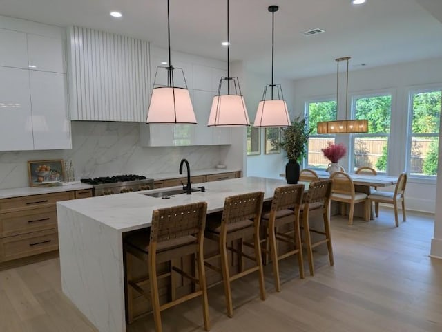 315 Hillcrest View Dr, Suwanee, GA 30024 - kitchen featuring a sink, light wood finished floors, backsplash, a kitchen island with sink, and hanging light fixtures