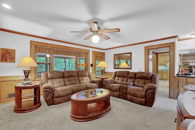 carpeted living area featuring ceiling fan, crown molding, wainscoting, and a textured ceiling