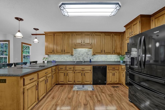 kitchen with black appliances, dark countertops, a peninsula, brown cabinets, and light wood finished floors