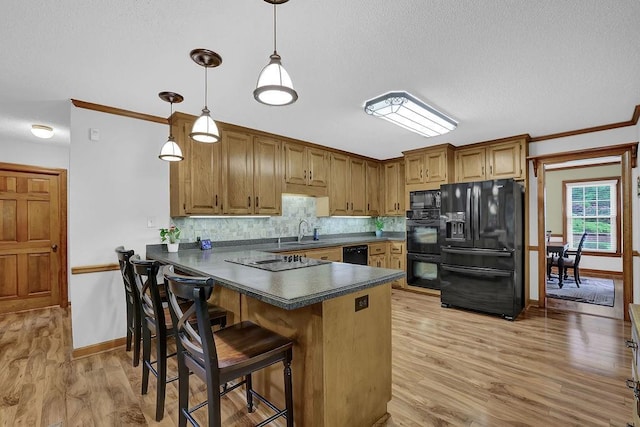 kitchen featuring black appliances, dark countertops, a peninsula, tasteful backsplash, and light wood-style floors