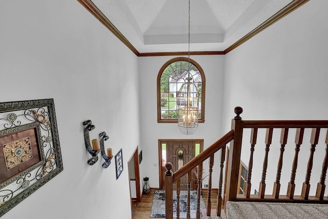 foyer with a chandelier, high vaulted ceiling, wood finished floors, baseboards, and crown molding