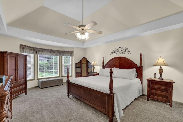 bedroom featuring a tray ceiling, light carpet, baseboards, and ceiling fan