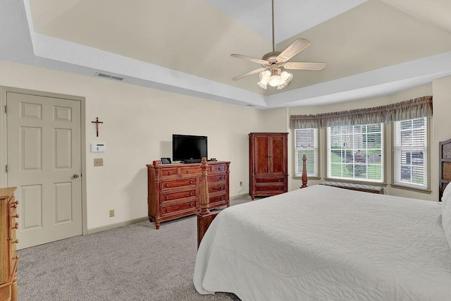 carpeted bedroom featuring a raised ceiling, baseboards, and a ceiling fan