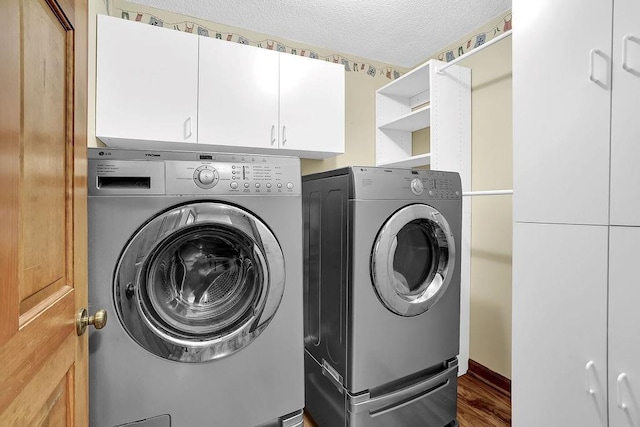 washroom with washing machine and clothes dryer, cabinet space, a textured ceiling, and wood finished floors