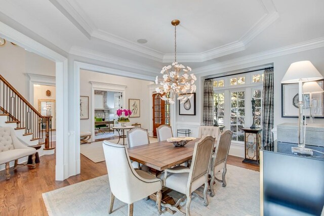 dining space with a raised ceiling, crown molding, and light hardwood / wood-style flooring