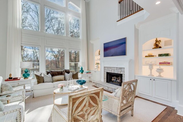 living room with hardwood / wood-style flooring, a stone fireplace, a towering ceiling, and a wealth of natural light