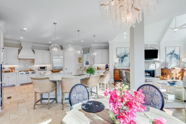 dining room featuring ceiling fan with notable chandelier, a stone fireplace, ornamental molding, and sink