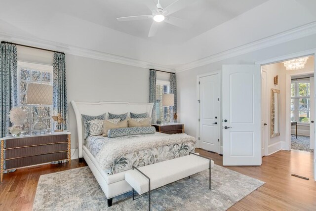 bedroom with hardwood / wood-style floors, ceiling fan with notable chandelier, a raised ceiling, and ornamental molding