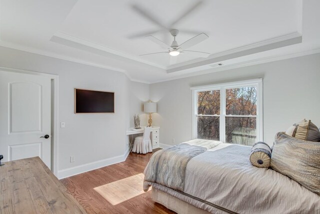 bedroom featuring ceiling fan, wood-type flooring, ornamental molding, and a tray ceiling