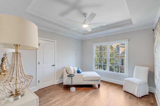 living area with a raised ceiling, ceiling fan, crown molding, and wood-type flooring