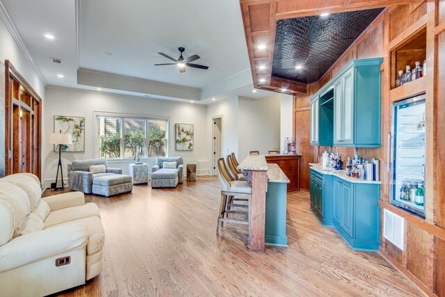 living room with a raised ceiling, bar area, ceiling fan, and light hardwood / wood-style floors