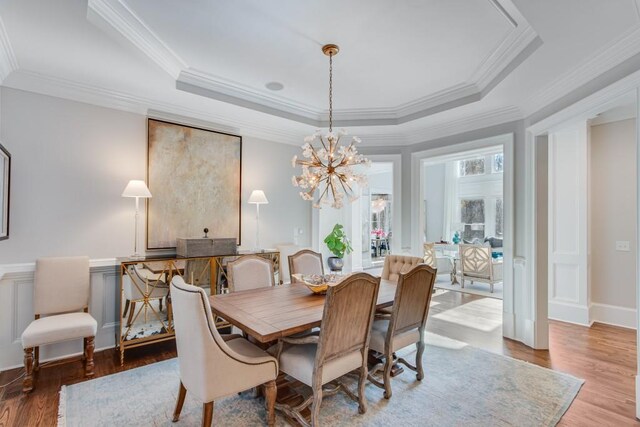 dining area with hardwood / wood-style floors, a tray ceiling, an inviting chandelier, and ornamental molding