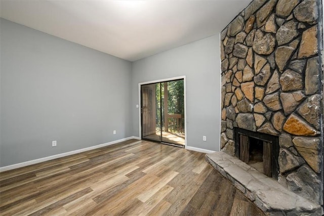 unfurnished living room featuring a stone fireplace, wood finished floors, and baseboards