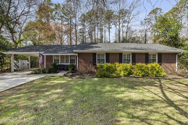 ranch-style house featuring concrete driveway, an attached carport, roof with shingles, a front lawn, and brick siding