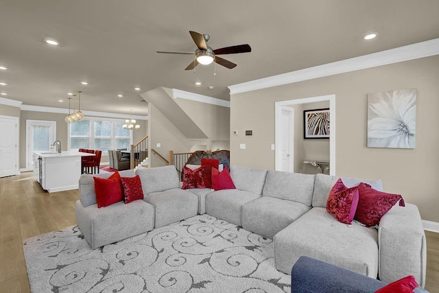 living room featuring crown molding, sink, ceiling fan with notable chandelier, and light hardwood / wood-style floors