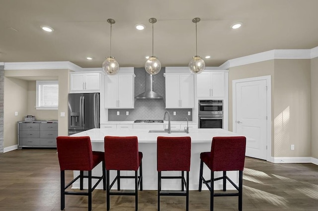 kitchen with stainless steel appliances, white cabinetry, a kitchen island with sink, and wall chimney range hood