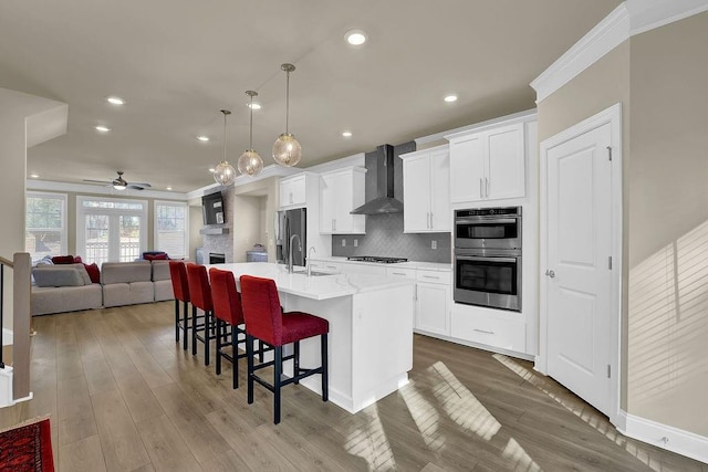 kitchen with a breakfast bar, pendant lighting, stainless steel appliances, a center island with sink, and wall chimney exhaust hood