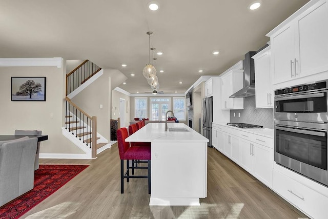 kitchen featuring appliances with stainless steel finishes, a breakfast bar, an island with sink, sink, and wall chimney range hood