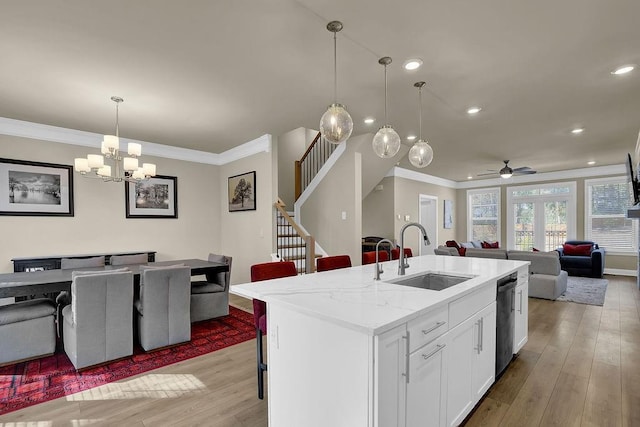 kitchen with sink, light hardwood / wood-style flooring, white cabinetry, light stone countertops, and a center island with sink