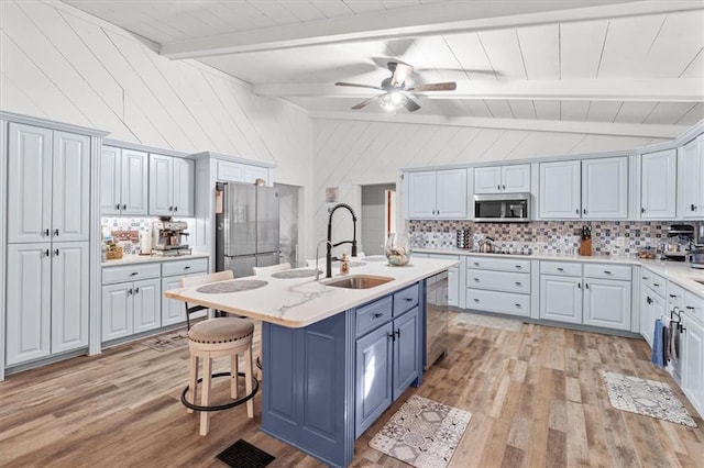 kitchen with a breakfast bar, decorative backsplash, a kitchen island with sink, and appliances with stainless steel finishes