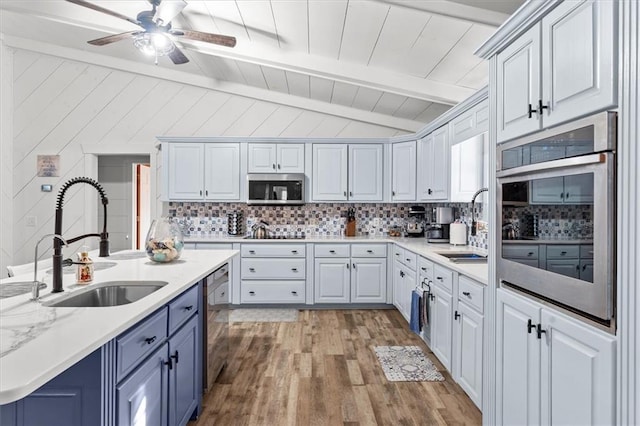 kitchen with sink, tasteful backsplash, light hardwood / wood-style flooring, lofted ceiling with beams, and appliances with stainless steel finishes