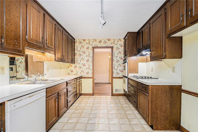 kitchen featuring wallpapered walls, under cabinet range hood, light floors, light countertops, and white appliances