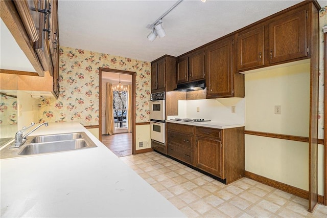 kitchen featuring a sink, wallpapered walls, double oven, light countertops, and light floors