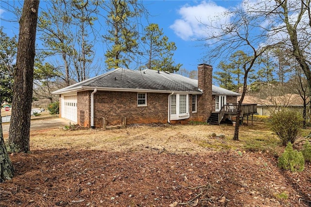 view of side of property with brick siding, a chimney, a garage, a deck, and driveway