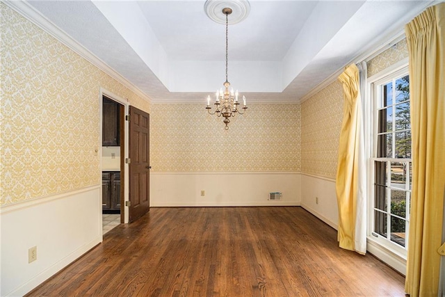 unfurnished room with wallpapered walls, a tray ceiling, wainscoting, wood finished floors, and a notable chandelier