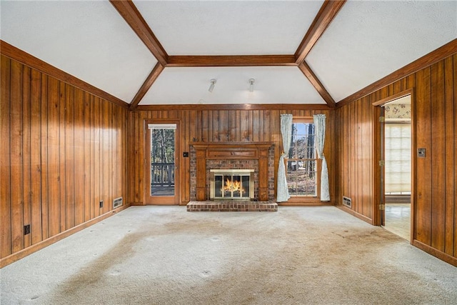 unfurnished living room with a wealth of natural light, lofted ceiling with beams, wood walls, and a fireplace