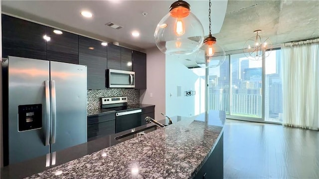 kitchen with pendant lighting, sink, appliances with stainless steel finishes, tasteful backsplash, and dark stone counters