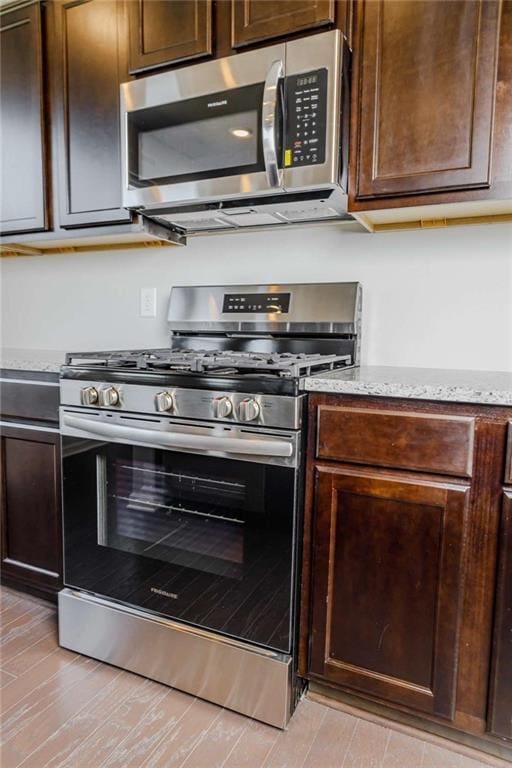 kitchen with stainless steel appliances, dark brown cabinets, and light stone countertops