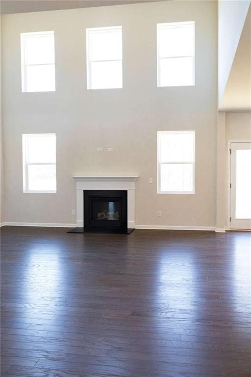 unfurnished living room with dark wood-type flooring, a glass covered fireplace, and a towering ceiling