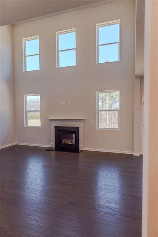 unfurnished living room with a fireplace with flush hearth, a towering ceiling, baseboards, and dark wood-style floors