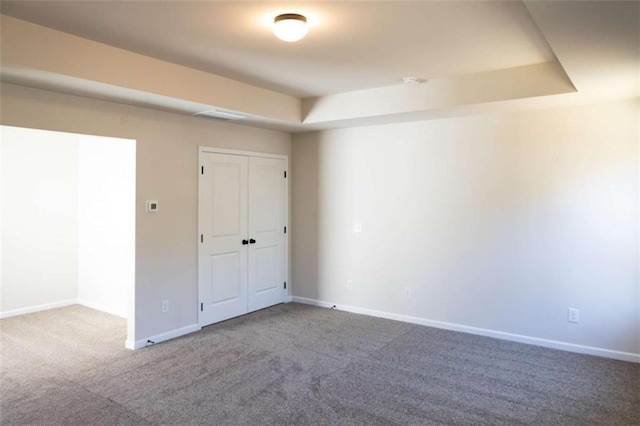 carpeted empty room featuring a raised ceiling and baseboards