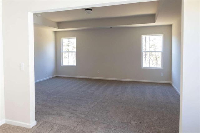 carpeted spare room with a tray ceiling and baseboards