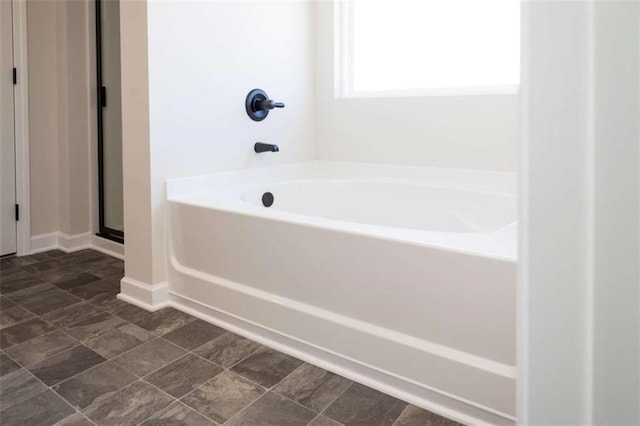 bathroom featuring a stall shower, a garden tub, and baseboards